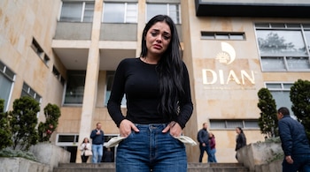 Una mujer llora frente al edificio de la DIAN mientras muestra los bolsillos de su pantalón vaquero vueltos hacia afuera.
