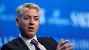 Primer plano de Bill Ackman, un hombre con cabello gris, traje oscuro y corbata estampada, hablando con la boca ligeramente abierta, contra un fondo azul borroso