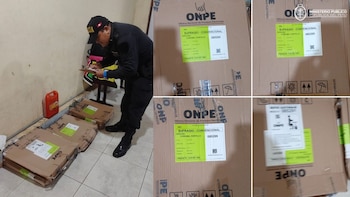 Un policía uniformado anota en un portapapeles junto a varias cajas de cartón de la ONPE, identificadas como material electoral, en un piso de baldosas