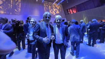 Varios hombres con traje formal posan sonrientes en un salón iluminado con luces azules durante una reunión social