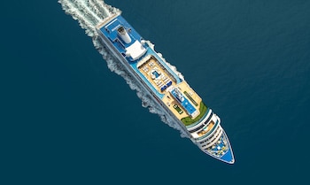 Vista cenital de un crucero blanco y azul navegando sobre agua azul oscura con una estela de espuma