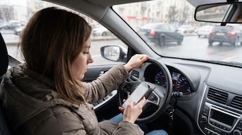 Una mujer en el asiento del conductor sostiene un teléfono celular frente al volante dentro de un automóvil.