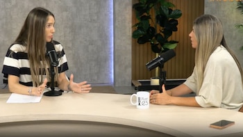 Dos mujeres sentadas a una mesa redonda frente a micrófonos de estudio y una taza blanca