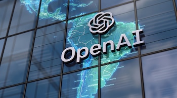 Logotipo tridimensional y texto de OpenAI colocados sobre el mapa de América Latina en la fachada de un edificio de vidrio.