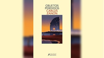 Portada del libro 'Objetos Perdidos' de Carlos Zañón. Muestra un edificio moderno con luz en las ventanas, un cielo anaranjado y morado, y una persona en la orilla del mar