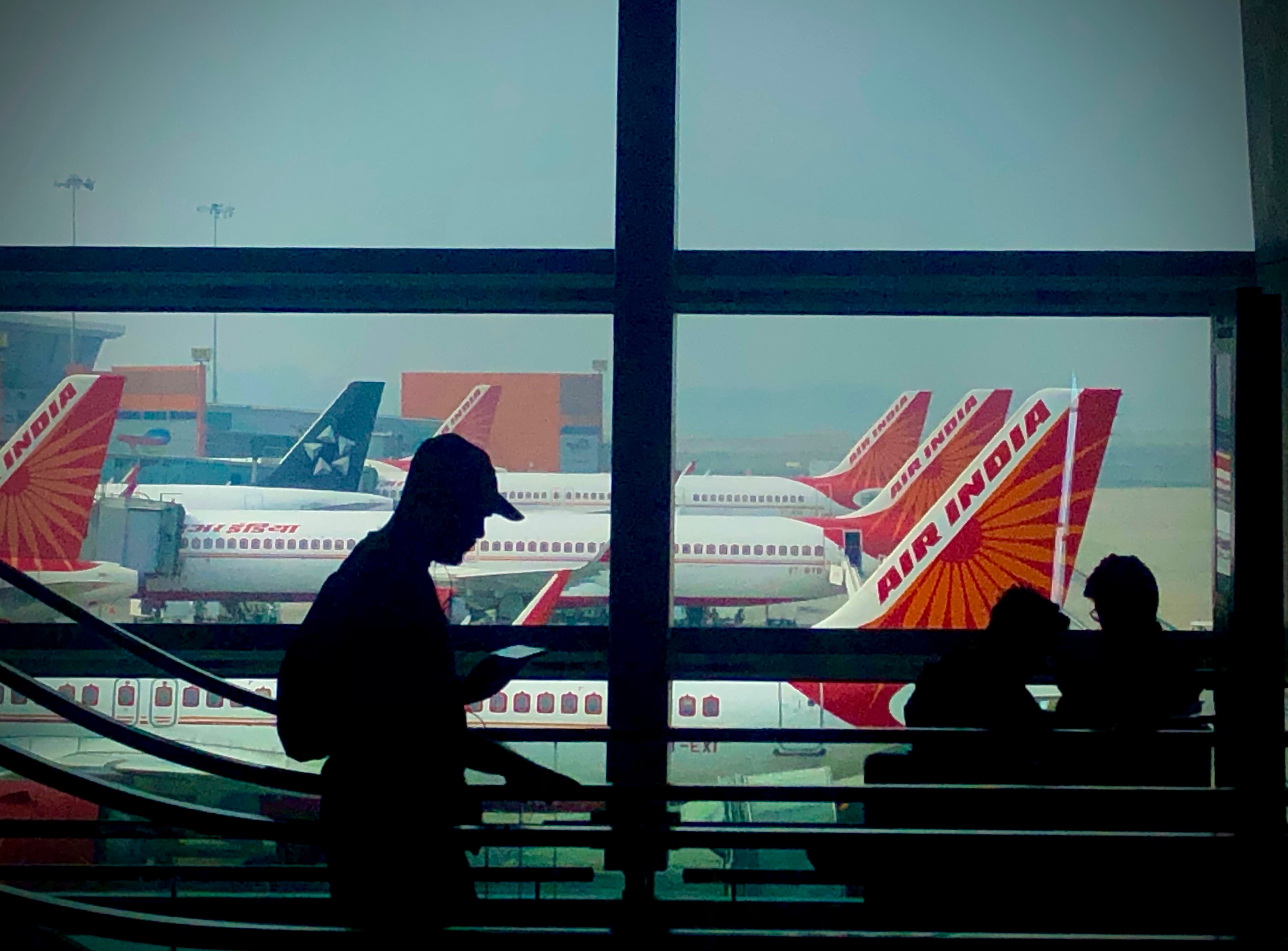 La silueta de un hombre se recorta contra un ventanal de un aeropuerto, con aviones de Air India de fondo, en Nueva Delhi, India. (AP Foto/Manish Swarup)