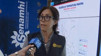 Una mujer con gafas y chaleco del Senamhi habla ante un micrófono junto a un mapa de récords de temperatura de Perú