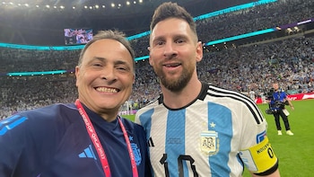 Lionel Messi, con camiseta argentina número 10, y otro hombre sonríen juntos en un estadio. Detrás, se observa el público y las luces brillantes del lugar