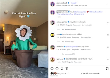 Giacomo Benavides, un hombre de piel clara, sonriendo y vestido con un disfraz de flor blanca y tallo verde, dentro de una maceta marrón, en una habitación de hotel
