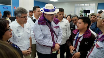 Grupo de personas, incluyendo al Presidente con sombrero de paja y camisa a rayas, escuchando a un joven en un centro de salud en Guatemala