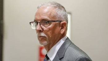 Primer plano de James M. Heaps, un hombre caucásico de mediana edad con cabello gris, gafas y bigote, mirando hacia la izquierda