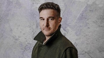 Primer plano de Jeffry Fischman, un hombre de tez clara con cabello oscuro y barba corta, vistiendo un abrigo verde oscuro, mirando a la cámara