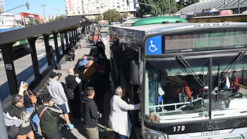 Vista elevada de una larga fila de personas esperando junto a la parada de un autobús plateado número 170 en una calle concurrida de la ciudad