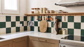 Cocina moderna con azulejos verdes y blancos, encimeras claras, gabinetes marrones, estante de madera con utensilios, frascos y un horno de inducción.