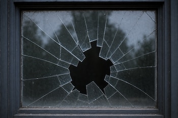 Un cristal agrietado con un orificio en el centro y fracturas radiales dentro de un marco de madera oscura.