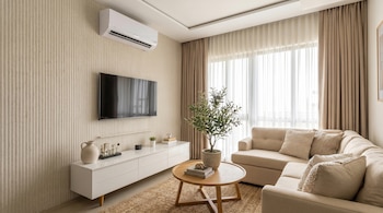 Vista frontal de una sala de estar moderna con sofá seccional beige, TV en pared texturizada, consola blanca, mesa de centro de madera y cortinas claras.