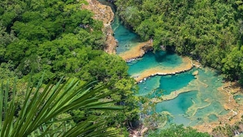 Vista aérea de Semuc Champey, mostrando piscinas naturales de agua turquesa escalonadas, rodeadas de exuberante selva y con personas nadando