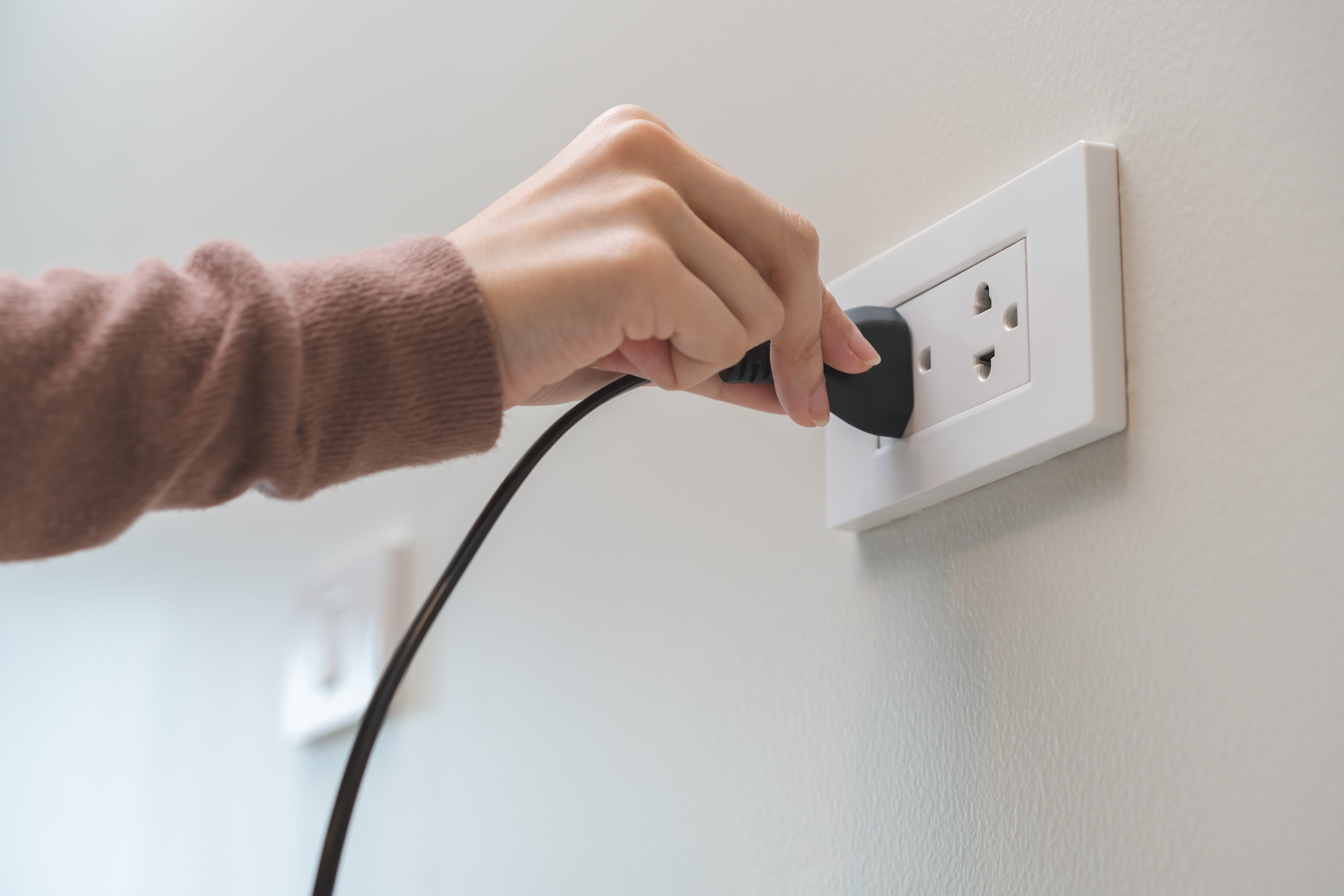 Mano de mujer que mete su cargador en un enchufe tradicional. (Freepik)