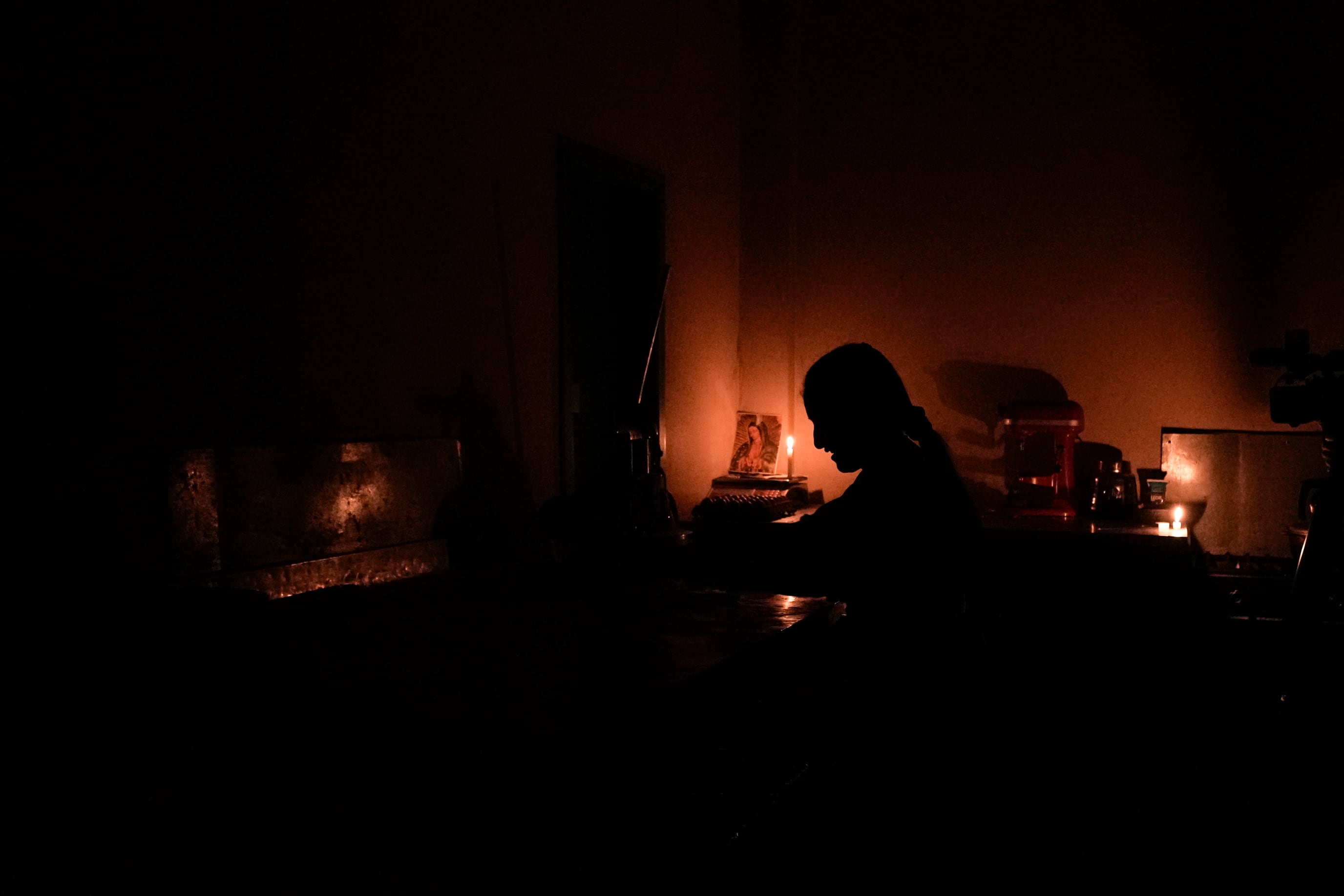 ARCHIVO - Mónica Valiente espera que lleguen clientes en su panadería, iluminada con una vela, durante un apagón eléctrico por racionamiento, el martes 15 de octubre de 2024, en Quito, Ecuador. (AP Foto/Dolores Ochoa, Archivo)