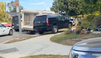 Patrullas policiales, una camioneta negra y una casa rodante estacionadas en una calle residencial delimitada con cinta policial amarilla