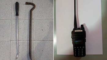Un radiotransmisor de mano Baofeng negro, una palanca recta plateada con mango negro y otra palanca curva oxidada, sobre una superficie bicolor
