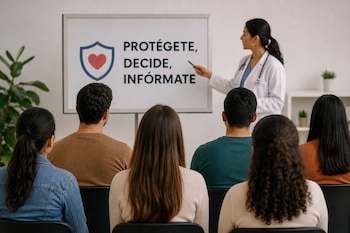 Una médica con bata blanca señala una pizarra con el texto Protégete, decide, infórmate frente a personas sentadas de espaldas.