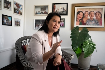 Keiko Fujimori sentada en una silla de mimbre, vistiendo un blazer claro y un collar con cruz, gesticulando con la mano derecha. Al fondo, un cuadro familiar y una planta grande