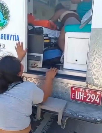 Ambulancia con la puerta lateral abierta y una persona mirando hacia el interior, donde se observa a un paciente en una camilla. La ambulancia lleva una placa de Perú