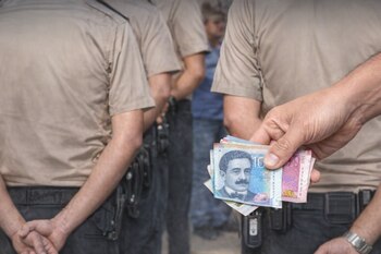 Una mano de hombre sujeta billetes de soles peruanos con denominaciones de 10 y 50 frente a tres personas con uniforme policial.