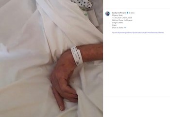 Primer plano de la mano de un hombre con una pulsera de identificación hospitalaria, descansando sobre sábanas blancas y arrugadas