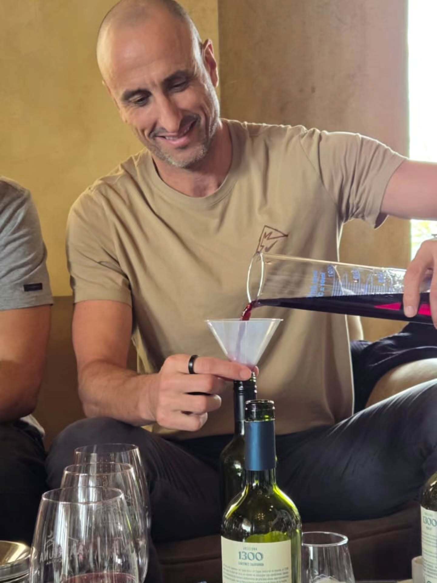 Manu Ginóbili vierte vino tinto con un embudo en una botella durante una experiencia enológica en Mendoza.