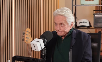 Un hombre de cabello canoso frente a un micrófono con el logotipo de SiriusXM, con un bajo eléctrico al fondo