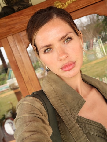 Primer plano de una mujer con chaqueta verde y cabello recogido que posa frente a un mueble de madera