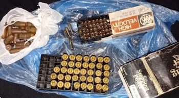 Vista aérea de una bolsa blanca con cartuchos grandes, una caja con municiones .22, una bandeja con cartuchos de pistola y una caja de .38 Special sobre plástico azul