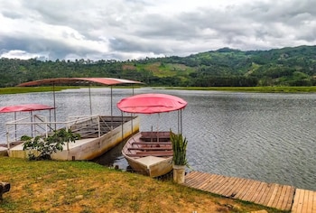 Tres embarcaciones con toldos rojos en la orilla de una laguna, junto a un muelle de madera. Al fondo se observan montañas con vegetación y un cielo nublado