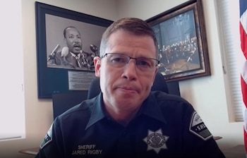 Un hombre con uniforme de sheriff y anteojos mira a la cámara en una oficina con un retrato de Martin Luther King de fondo