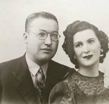 Fotografía en blanco y negro de un hombre con traje, camisa, corbata y gafas, junto a una mujer con peinado recogido, pendientes y top de encaje
