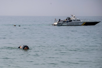 Una persona nada en el agua con flotador y aleta, y al fondo una lancha blanca de la Guardia Civil con varios tripulantes a bordo