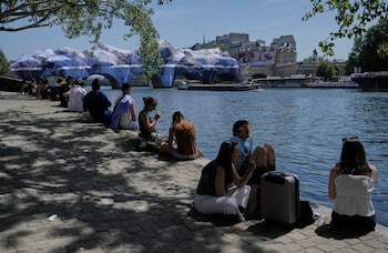 Parisinos buscan alivio del calor a orillas del Sena, con una obra del artista callejero JR sobre el Puente Nuevo de fondo, un día antes de que Francia registrara su temperatura más alta en un mes de mayo desde que hay registros. (AP Photo/Michel Euler)