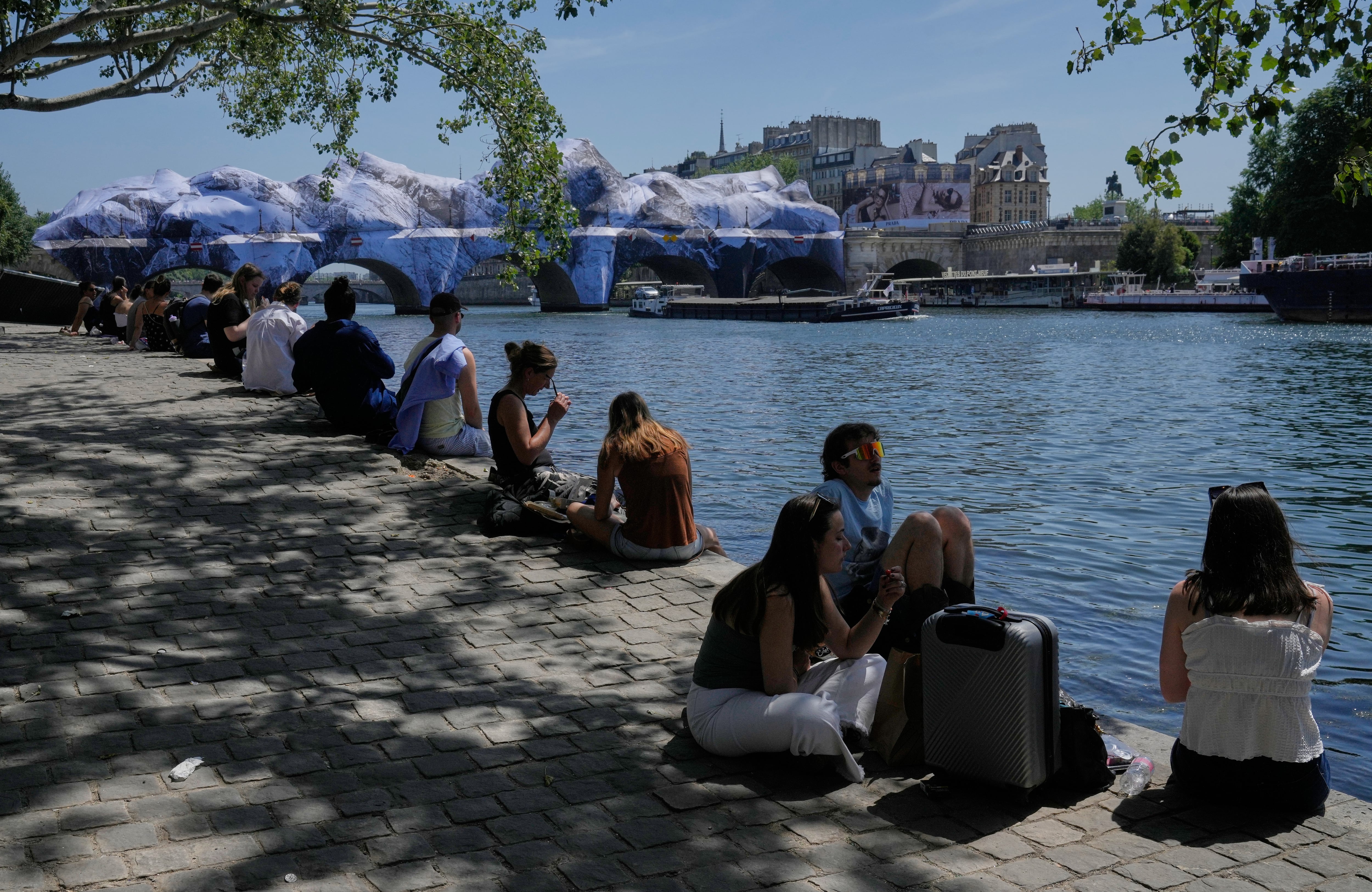 Parisinos buscan alivio del calor a orillas del Sena, con una obra del artista callejero JR sobre el Puente Nuevo de fondo, un día antes de que Francia registrara su temperatura más alta en un mes de mayo desde que hay registros. (AP Photo/Michel Euler)