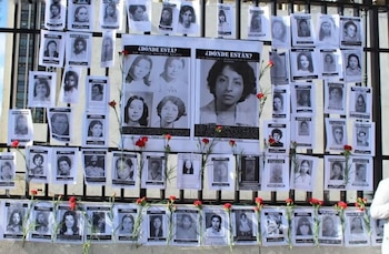 Decenas de carteles con fotografías en blanco y negro de personas y claveles rojos colocados sobre una reja metálica