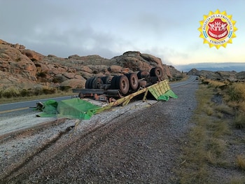 Un camión de carga volcado sobre el costado de una carretera de montaña flanqueada por rocas y vegetación baja