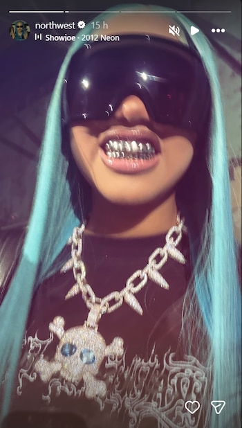 Primer plano de una persona con pelo azul brillante, grandes gafas de sol oscuras, grillz plateados y un collar con colgante de calavera enjoyado