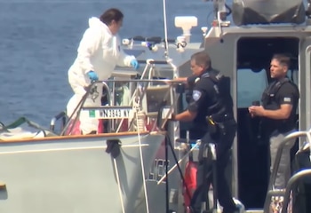 Una persona con traje blanco protector y dos agentes de policía en dos embarcaciones. Una embarcación tiene la matrícula WN 3843 NY y la palabra "POLICE"