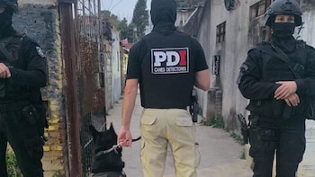 Tres personas con uniforme táctico oscuro, máscaras y cascos en un pasaje. Una persona lleva camiseta con el logo 'PDI Canes Detectores' y un perro negro con correa
