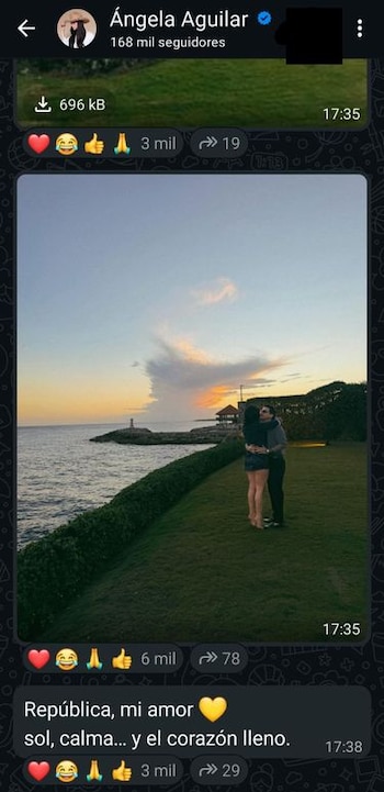 Una mujer abraza a un hombre de espaldas frente al mar al atardecer. Un faro y un cenador se observan a lo lejos sobre una costa rocosa
