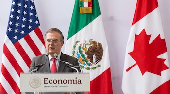 Un hombre de traje y corbata roja habla en un podio con el logotipo de la Secretaría de Economía, flanqueado por las banderas de Estados Unidos, México y Canadá.