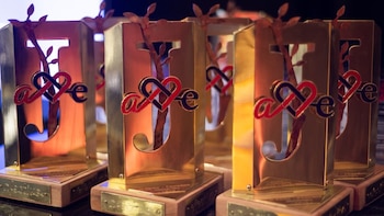 Múltiples trofeos dorados con bases de madera. Cada uno tiene la letra 'J' calada con un tronco y hojas, y las letras 'a', un corazón y 'e' entrelazadas