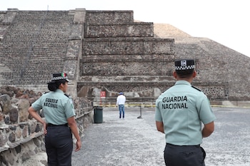 Dos agentes de la Guardia Nacional, uno de espaldas y otro de perfil, patrullan frente a grandes pirámides de piedra en Teotihuacán, con un turista al fondo