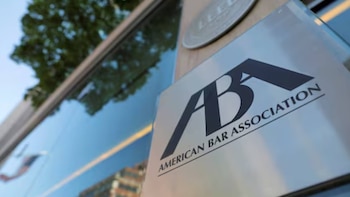 Placa plateada de la American Bar Association con logo y nombre en la fachada de un edificio. Reflejos del cielo azul y un árbol en el cristal